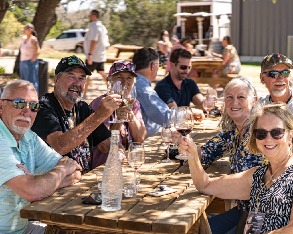 A large group around a long table on the reserve, raising their glasses together