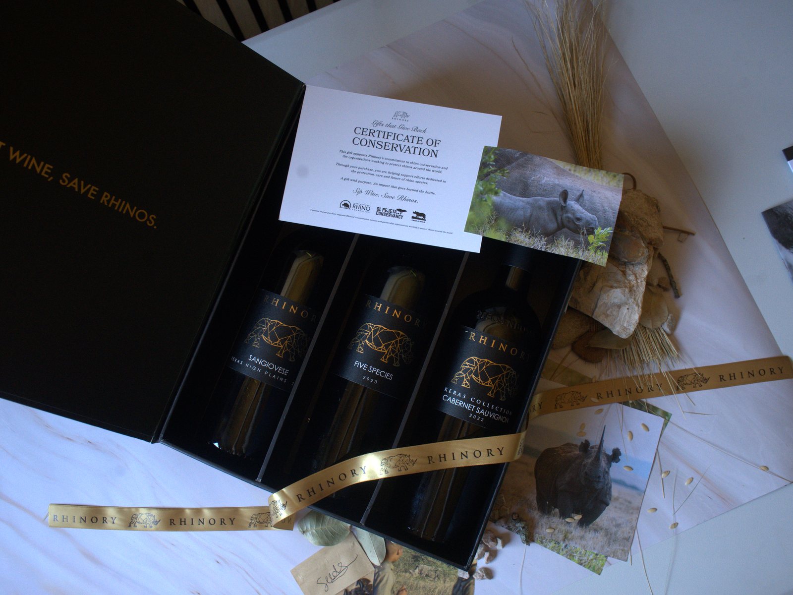 An open Rhinory gift box with a Certificate of Conservation, a rhino photo card and a gold Rhinory ribbon